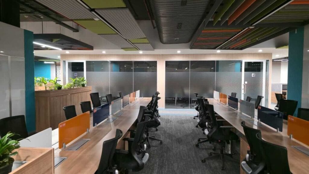Spacious office meeting room featuring desks, chairs, and glass walls for collaboration.